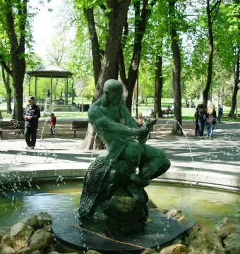 Fisherman Fountain bronze statue of a man wrestling a serpentine creature in a park with trees and paths.