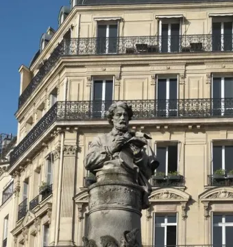 Gavarni Fountain with a stone bust of a bearded man writing in a book atop a carved cylindrical pillar.