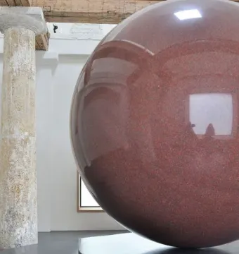 Large Red Sphere sculpture on a two-tiered circular pedestal in a bright interior space.