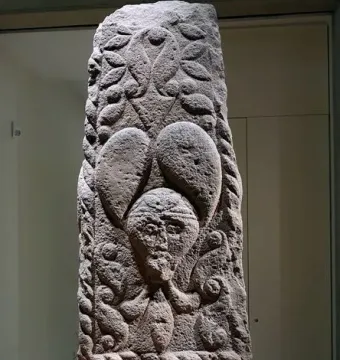 Pfalzfeld Obelisk with carved foliage patterns and three human faces on a stone column.