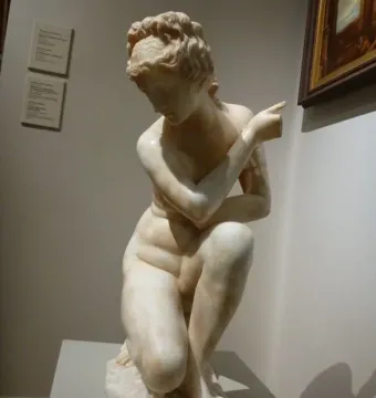Crouching Venus marble statue of a crouching nude female figure displayed on a pedestal in a gallery