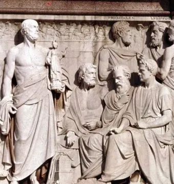 Stone relief from the Frieze of Parnassus showing classical sculptors in draped robes, including bearded figures in profile.