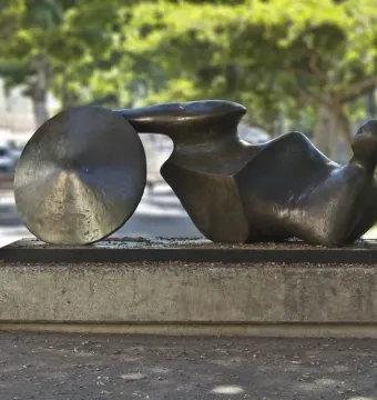 The Goslar Warrior bronze sculpture in an outdoor setting, shown as a dark abstract recumbent figure with a round disc form at one end.