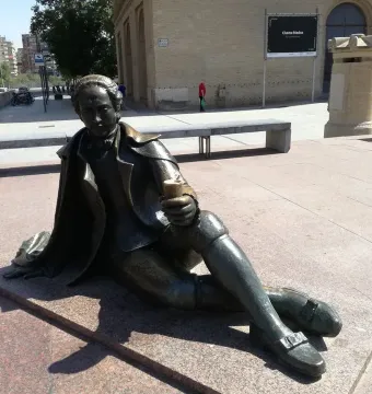 The Goya Memorial bronze statue sits on a low granite platform in a sunny public square.