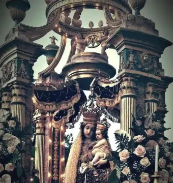 Crowned Madonna dell\'Udienza statue of the Virgin Mary with the infant Jesus, set in an ornate gilded shrine with roses, lilies, and candles.