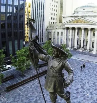 Maisonneuve Monument bronze statue on a stone pedestal fountain in a public square, with high-rise buildings and a domed classical building nearby.