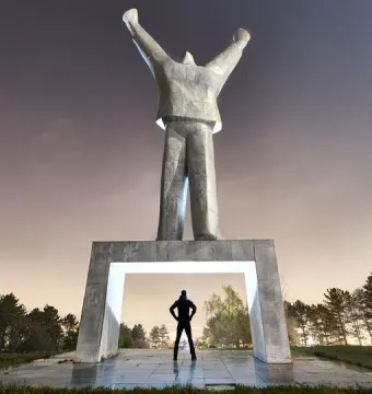 Monument to Stjepan Filipović, a tall abstract concrete statue with raised arms above a lit pedestal arch and silhouetted figure.