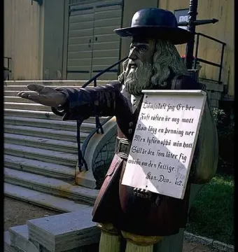 Rosenbom, a wooden statue of an old man with a beard and dark hat holding a sign across his chest.