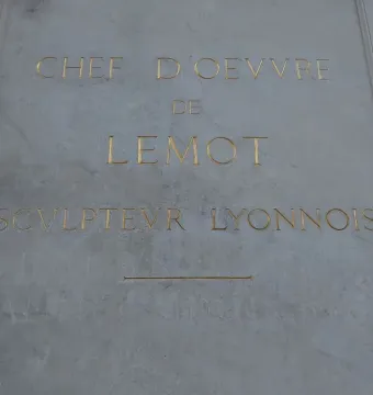 Close-up of a carved stone inscription panel on the Louis XIV equestrian statue, with gold-lettered text and a decorative line.