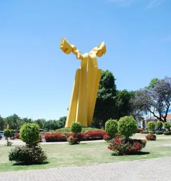 Ángel Custodio, a tall yellow abstract sculpture with curved wing-like shapes in a park.