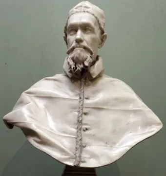 White marble bust of Pope Innocent X with a bearded face, cap, and decorated collar on a dark pedestal.
