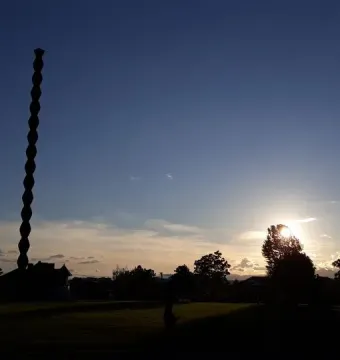 The Endless Column silhouetted against a bright evening sky with trees and grass in the foreground.