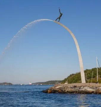 God our Father on the Rainbow sculpture with water arcing into the bay beside a rocky shoreline