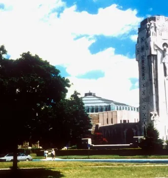 The National Shrine of the Little Flower with a tall stone tower and Christ figure beside a rounded building, framed by trees and a grassy foreground.