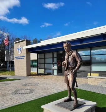 The Ideal Scout bronze statue on a stone pedestal outside a modern building with a blue sign and American flag.