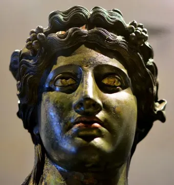 Close-up of the bronze head of Tiber Dionysus with wavy hair, a grape wreath, and inlaid eyes.