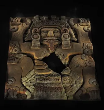 Tlaltecuhtli Monolith with a fanged mouth, elaborate headdress, and clawed limbs in reddish-brown stone.