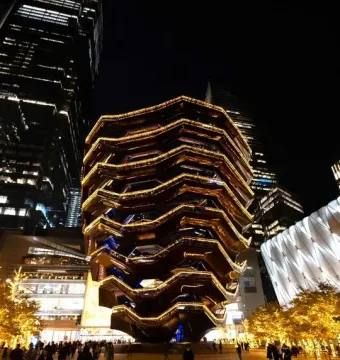 The Vessel glowing with golden lights at night, with people gathered around its base.