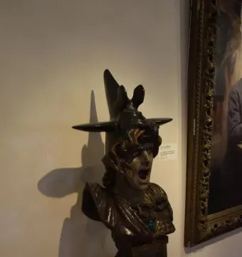 Bellona bust with a winged helmet and open mouth displayed on a white pedestal.