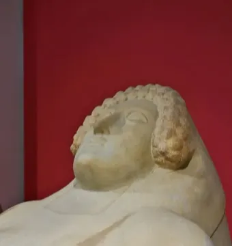 Stone head of the Lady of Cádiz sculpture with curled hair and a serene face against a red background.