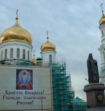 Monument to Dimitry of Rostov in front of a church with golden domes and a bell tower under restoration netting.