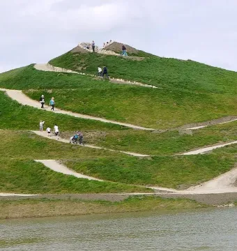 Northumberlandia’s grassy sculpted hill with winding paths and people walking along the slopes beside water.
