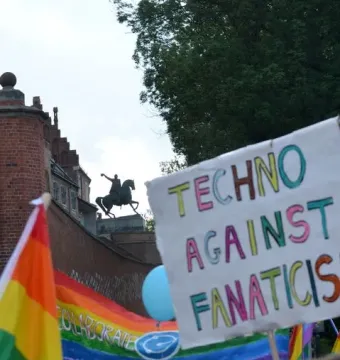 Tadeusz Kościuszko Monument seen as a dark silhouette atop a brick bastion above a colorful crowd and protest banners.
