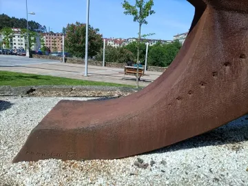 Dorna sculpture with a rust-colored textured curved form resting on white pebbles in a city square.