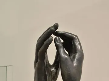 The Cathedral sculpture showing two dark metal hands rising upright with fingertips nearly touching.