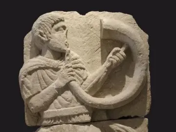 Broken stone relief of the Acrobat from Osuna showing a male figure playing a horn.
