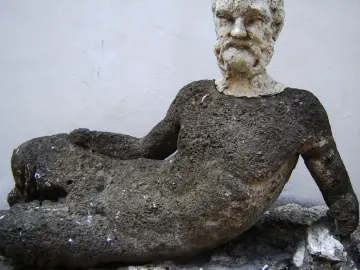 Weathered reclining figure on the Babuino Fountain, with a dark textured body and lighter bearded head.