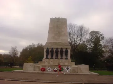 Guards Memorial with five dark soldier statues, floral wreaths at the base, and a runner in red passing by.