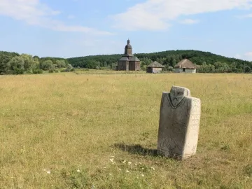 Kernosivka Idol stone monument standing in a grassy field with a church and trees in the background.