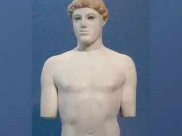 Kritios Boy marble statue of a nude young male figure against a blue background, missing its arms and part of one leg.