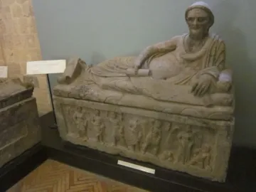 Sarcophagus of Laris Pulenas with a reclining male figure on the lid and carved relief figures along the base.