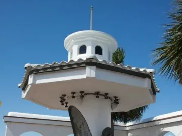 Mirador de la Flor monument with Selena Quintanilla statue, tribute plaque, and rose beside a bay railing.