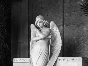 Monteverde Angel marble sculpture standing before the Oneto tomb with wings spread and head bowed.