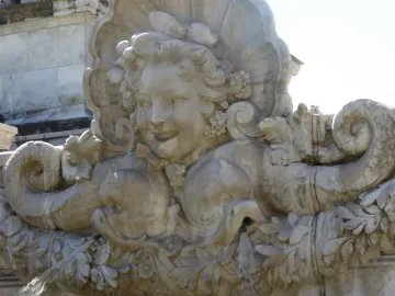 Ornate stone fountain from the Monument aux Girondins with a smiling female face, shell motifs, and sea creatures spouting water.