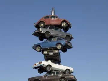 Spindle sculpture in Berwyn, Illinois, with eight cars stacked on a vertical spike against a clear blue sky.