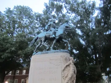 Stonewall Jackson equestrian statue on a stone pedestal surrounded by bushes and trees.