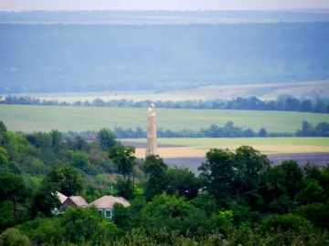 Thanksgiving Candle monument standing in a green field with a cross and flame-like top.