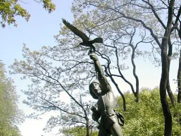 The Falconer bronze statue on a stone pedestal among trees in Central Park.
