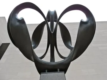Continuum, a dark metal sculpture with upward-curving symmetrical loops on a pedestal against a stone wall, seen from below.