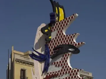 The Face of Barcelona sculpture with red dots, yellow-and-black stripes, and blue mosaic tiling against a blue sky.