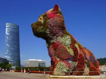 Jeff Koons’ Puppy topiary sculpture covered in flowers, with a skyscraper and city buildings behind it.