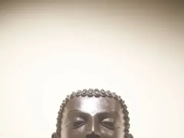 Head and shoulders of the Sultanganj Buddha with curly hair, downcast eyes, and elongated earlobes