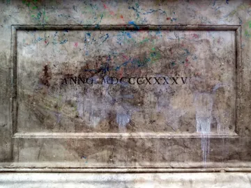 Weathered stone plaque from the Canapone monument with Roman numerals and paint splatters.