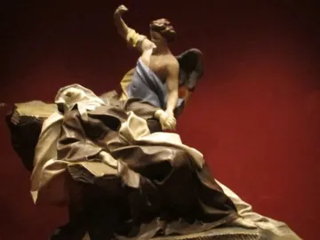 Terracotta sculpture of the Ecstasy of Saint Teresa showing a reclining robed figure and a winged angel above against a red background.
