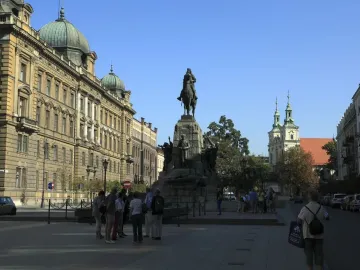 Grunwald Monument with an equestrian statue on a stone pedestal in a city square, with historic buildings and people nearby.