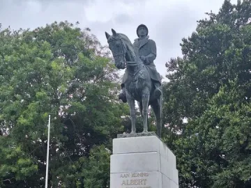 Bronze equestrian statue of King Albert I on a stone pedestal in a park, with trees and a few people in the background.